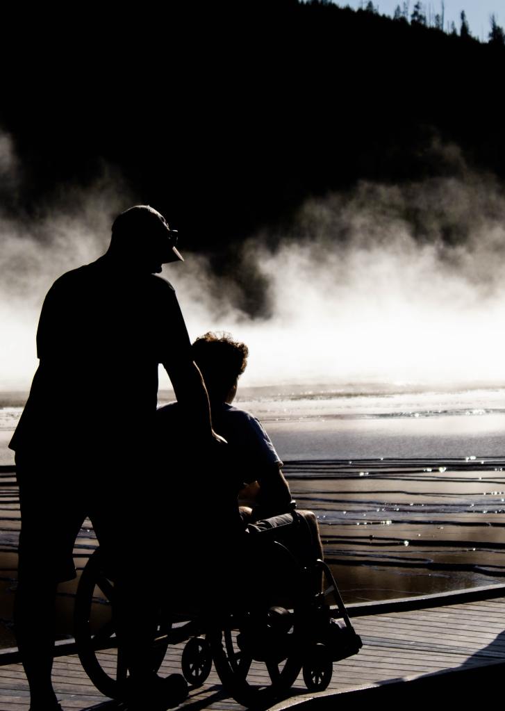 Image of a man pushing another man in a wheelchair along a boardwalk.