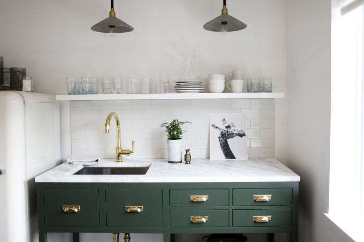 Image shows dark green kitchen cabinets and sink, with open space beneath sink. Links to Remodelista website.
