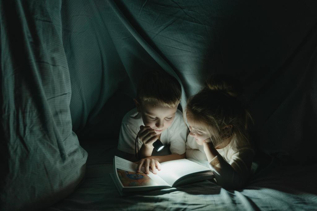 Image of boy and girl reading in blanket fort. 